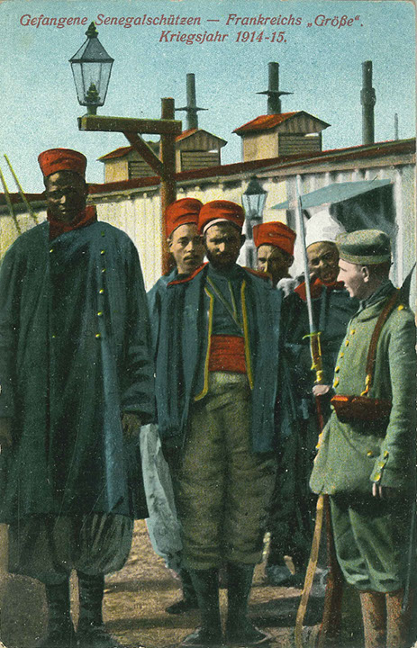 "Gefangene Senegalschützen – Frankreichs „Größe“. Kriegsjahr 1914-15". Ansichtskarte, gesendet aus (Köln-) Wahn (Schießplatz) als Feldpost im Oktober 1915. Sammlung Detlev Brum. Es ist nicht bekannt, in welchem Gefangenenlager das Bild produziert wurde. Die gleiche Ansichtskarte ist etwa im Februar 1916 vom Truppenübungsplatz Heuberg (Schwäbische Alb), dort befand sich ebenfalls Gefangenenlager, versendet worden. Drei unterschiedliche Ansichtskarten zeigen denselben "Senegalschützen" und diese Ansichtskarten sind deutschlandweit als Feldpost oder privat versendet worden.