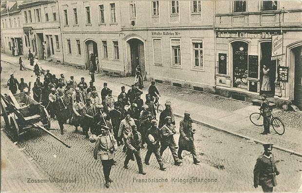 "Französische Kriegsgefangene. Zossen-Wünsdorf". Ansichtskarte mit französischen Kolonial-Soldaten, als Feldpost gelaufen im März 1917 (Infanterie-Regiment 49). Sammlung Markus Kreis. Öffentliche Märsche in die Kriegsgefangenenlager wurden als Zeichen des Sieges gerne für Ansichtskarten genutzt.