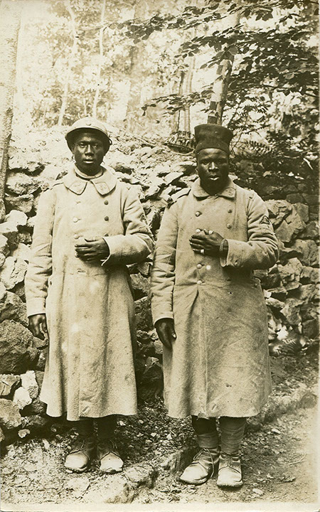 Ansichtskarte, ungelaufen, ohne Datum, keine weiteren Angaben. Sammlung Markus Kreis. Die Ansichtskarte zeigt zwei kriegsgefangene afrikanische Soldaten, die als Trophäe inszeniert werden. Jeweils die linke Hand, an der die Soldaten Ringe und Armband tragen, wird demonstrativ hervorgehobenen. Ringe und Armbänder sind zeitgenössisch als Teil der deutschen Propaganda zu verstehen, die mit dem Vorwurf propagandistische Wirkung zu erzielen suchte, das die kolonialen Soldaten das Kriegsvölkerrecht missachteten und Finger, Ohren und Köpfe der Feinde abschnitten und/oder Ringe und Armbänder entwendeten. In der Realität sind jedoch keine ungewöhnlichen Verstöße gegen das Kriegsvolkerrecht bekannt geworden.