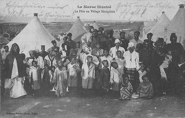"Le maroc illustré. La Fête au Village Sénégalais" (Ein Fest in einem senegalesischen Dorf). Carte Postale, gelaufen als Kriegsgefangenenpost im Januar 1916 aus dem Kriegsgefangenenlager Kenitra in Marokko an die Ehefrau nach Deutschland. Sammlung Detlev Brum. Ob es sich tatsächlich um eine Szene in einem senegalesischen Dorf handelt, ist unklar. Die abgebildeten Zelte ähneln den Zelten, die das Rote Kreuz in den Kriegsgefangenenlagern fotografierte. Nutzen Afrikaner hier die Möglichkeit, sich die deutschen Kriegsgefangenen im Lager anzuschauen? Oder doch nur ein Besuch der Angehörigen in einem Ausbildungslager in Marokko?