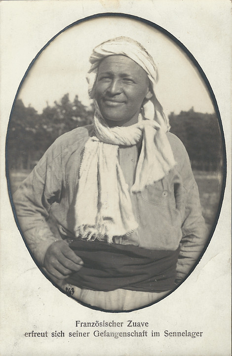 "Französischer Zuave erfreut sich seiner Gefangenschaft im Sennelager". Ansichtskarte, gelaufen im Oktober 1914 von Sennelager nach Düsseldorf (Vater an Tochter). Sammlung Detlev Brum. Eine freundliche Fotografie, die durch den Text ironisiert wird. Kriegsgefangenschaft ist niemals erfreulich, speziell in der ersten Phase nach Kriegsbeginn sind die Verhältnisse in den Kriegsgefangenenlagern katastrophal.