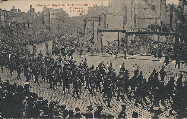 "Gefangenentransport in Lille 1915 (Schotten, Engl., Franzosen und Farbige)". Ansichtskarte, ungelaufen. Sammlung Detlev Brum. Die Ansichtskarte zeigt einen langen Zug von Kriegsgefangenen, der durch das schwer kriegszerstörte Lille (Nordfrankreich) geführt wird.