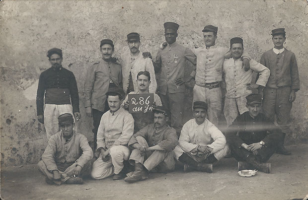 Ansichtskarte ohne Titel. Afrikanischer Soldat mit Orden unter französischen und afrikanischen Waffenbrüdern. Carte Postale, gelaufen nach Paris, ohne Datum. Sammlung Detlev Brum. Vermutlich handelt es sich um eine Ansichtskarte, die eine gemischte Armee-Einheit von französischen und afrikanischen Soldaten darstellt. Im Mittelpunkt steht der ordensgeschmückte afrikanische Soldat.