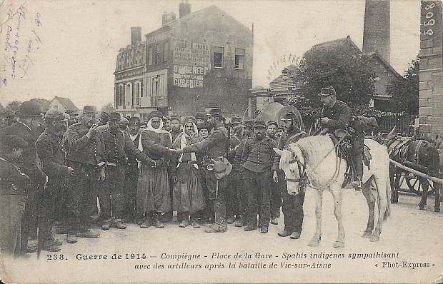 "Guerre de 1914 – Compiègne – Place de la Gare – Spahis indigénes sympathisant avec des artilleurs après la bataille de Vic-sur-Aisne" (Eingeborene Spahis sympathisieren (verbrüdern sich) mit Artilleristen nach der Schlacht von Vic-sur- Aisne). Carte Postale beschriftet in französischer Sprache mit Datum vom Januar 1915. Sammlung Detlev Brum Compiègne ist eine Stadt in Nordfrankreich; in Compiègne wurde der erste Waffenstillstand geschlossen, der den Ersten Weltkrieg beendete.